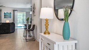 A modern living room with a white console table, a gold lamp, and a blue vase with green plants. - Last Minute Disney! Private Pool, Hot Tub & Themed Bedrooms. Book Now! #105265 (Orlando)