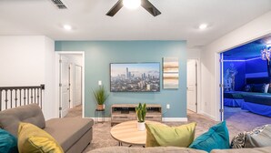 A living room with a gray sofa, a round coffee table, and a cityscape painting on the wall. - Last Minute Disney! Private Pool, Hot Tub & Themed Bedrooms. Book Now! #105265 (Orlando)