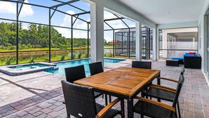 An outdoor patio with a pool, wicker furniture, and a view of a house and greenery.