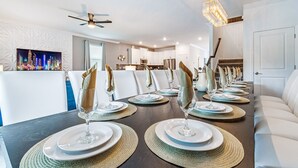 A dining area with a long table set for a meal, a ceiling fan, and a cityscape painting on the wall.