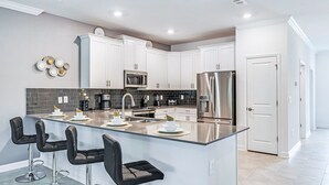 A modern kitchen with white cabinets, a stainless steel refrigerator, a microwave, and a large island with bar stools.