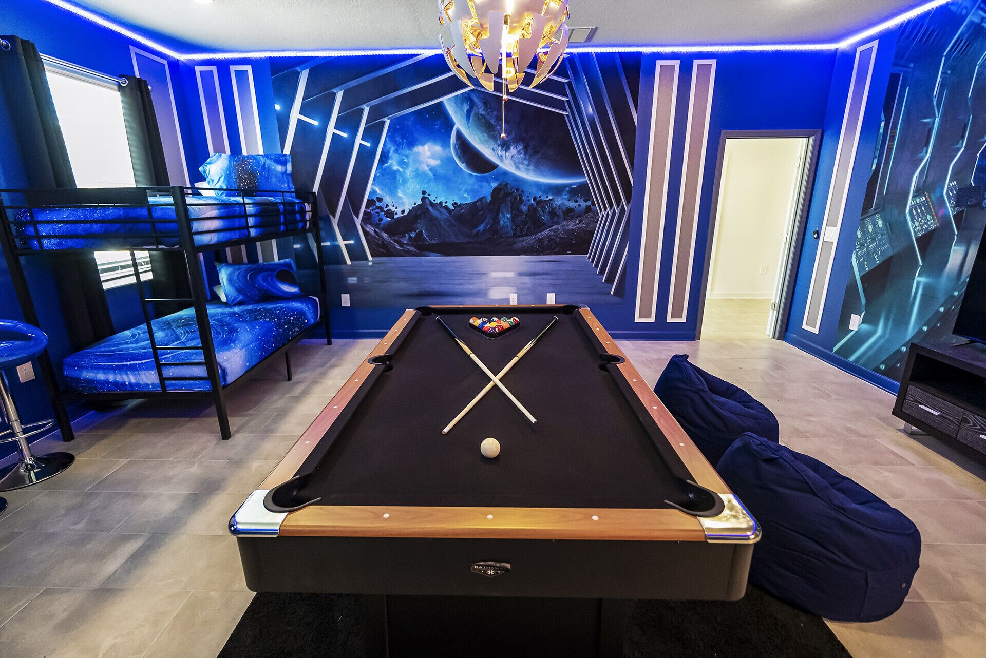 A pool table in a room with a blue and black color scheme, a bunk bed, and a large mural of space.
