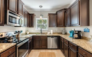 A kitchen with dark wood cabinets, stainless steel appliances, a granite countertop, and a welcome sign. - Spacious Home + Pool, Nearby Beach, Grill & Bikes (Inlet Beach)