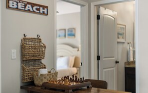A chessboard on a wooden table with wicker baskets and a sign that reads 'WELCOME TO THE BEACH'. - Spacious Home + Pool, Nearby Beach, Grill & Bikes (Inlet Beach)