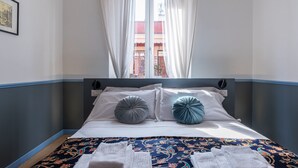 Un letto rifatto con cura, coperto da una trapunta fantasia, due cuscini e una finestra con tende.