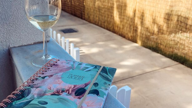 A planner on a table with a glass of white wine, overlooking a coastal area with buildings and a clear sky. - Asteria Apartments (Hersonissos)