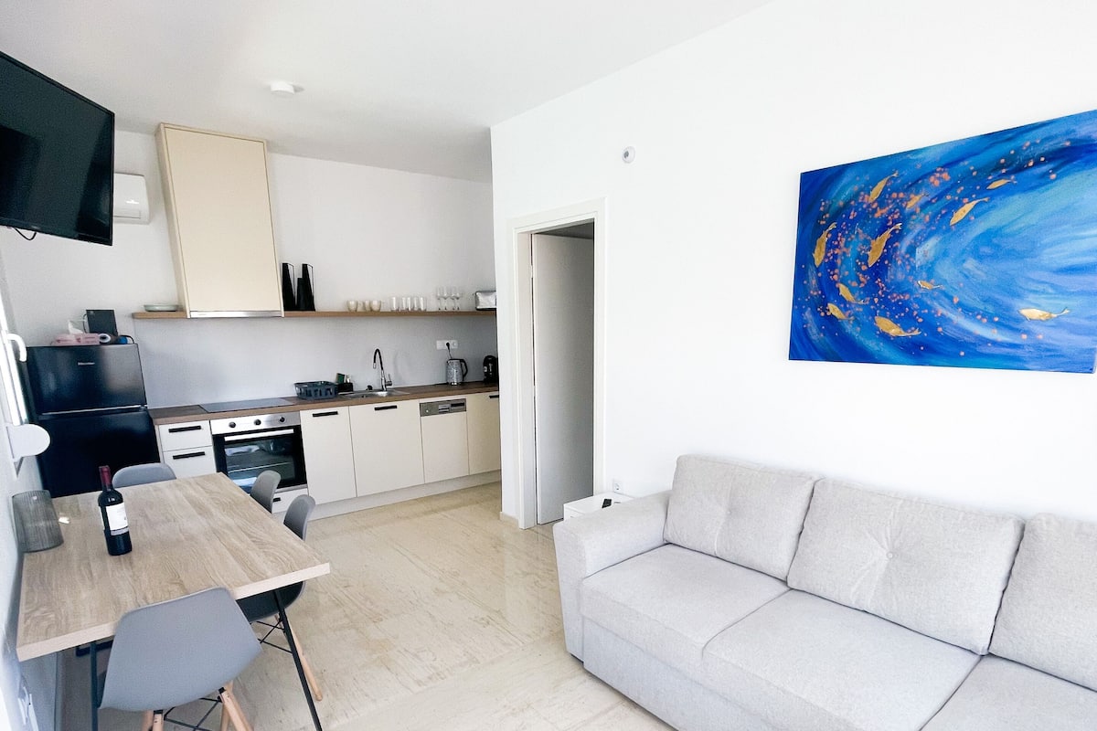 Eine moderne Küche mit weißen Schränken, einem Esstisch mit Stühlen und einem grauen Sofa.