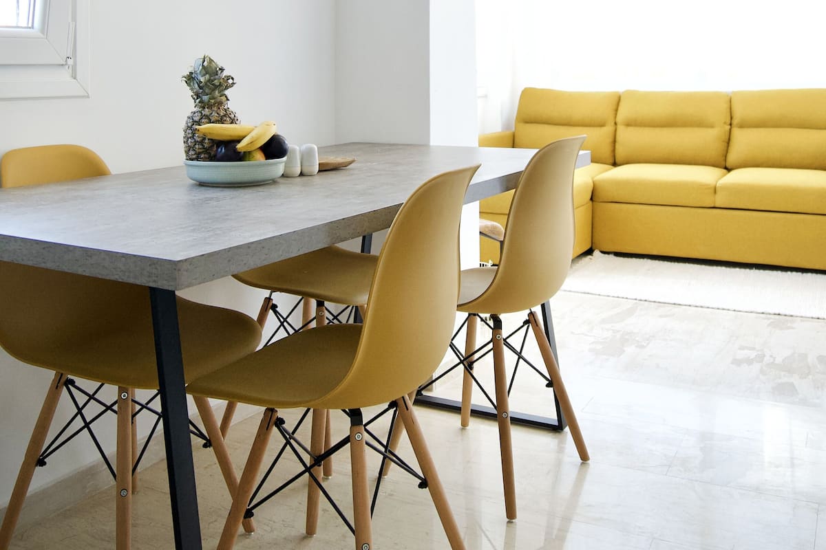 Ein moderner Essbereich mit einem grauen Tisch, gelben Stühlen und einem gelben Sofa im Hintergrund.