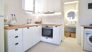 A compact kitchen with white cabinets, a built-in oven, a coffee maker, and a washing machine. - Asteria Apartments (Hersonissos)