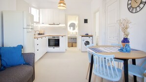 A compact kitchen with a dining area, a sofa, and a clock on the wall. - Asteria Apartments (Hersonissos)