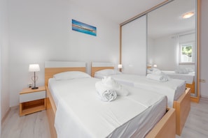 Et hotelværelse med to senge, et natbord med lampe, et maleri på væggen og et stort spejl.