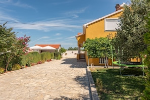 A stone-paved driveway leading to a yellow building with a red-tiled roof, surrounded by greenery and a clear sky. - Villa Bellezza Zadarvillas (Galovac)