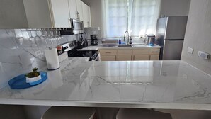 A modern kitchen with a marble countertop, stainless steel appliances, and a window with curtains. - Amazing beachfront apartment on the beach (Río Grande)