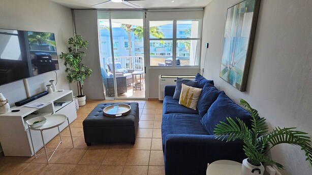 A modern living room with a flat-screen TV, a dark blue sofa, a small round table, and a potted plant. - Amazing beachfront apartment on the beach (Río Grande)
