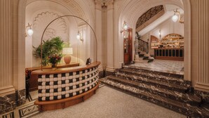 A grand lobby with a checkered bench, a reception desk, and a staircase leading to a bar area. - Hotel Fleur de Ville (Brussels)