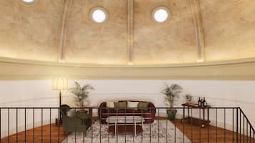 A spacious room with a high ceiling, a round table, a sofa, and two potted plants.