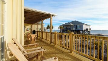 Une terrasse en bois avec des bancs donnant sur la plage, un espace couvert et une maison en arrière-plan.