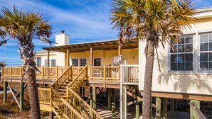 A wooden structure with a staircase leading to a deck, surrounded by palm trees. - Festive Beach House Steps from the Ocean! - Coconut Breeze (Dauphin Island)