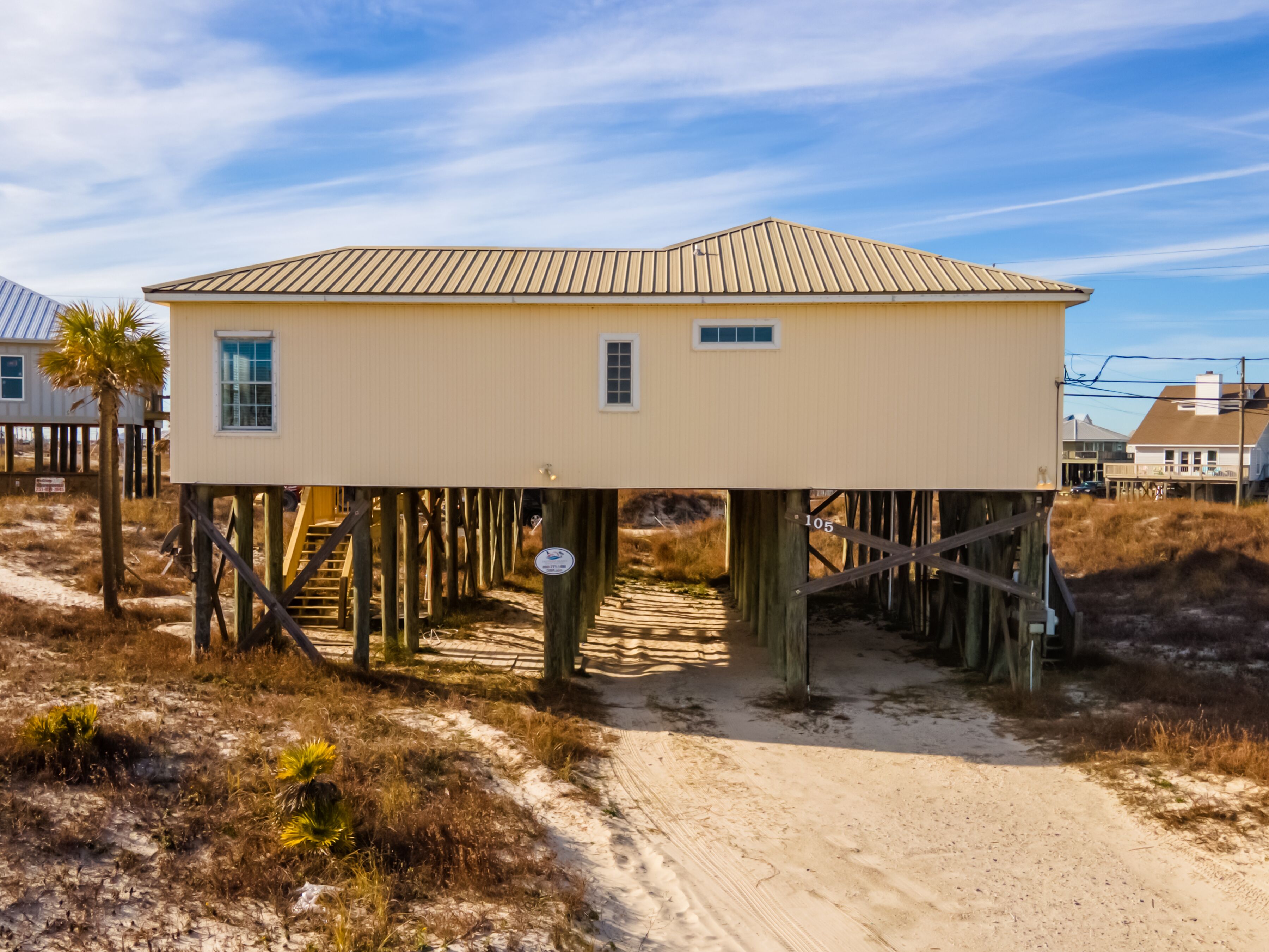 Una casa davant del mar, alçada sobre pilars, amb un camí de sorra que hi condueix.