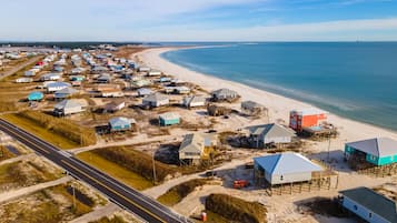Une vue aérienne d’une zone côtière avec de nombreux bâtiments, dont certains sont surélevés sur des piliers, et une route qui longe la plage.