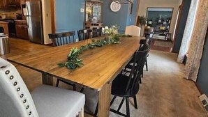 Un comedor con una larga mesa de madera, sillas negras y una araña.