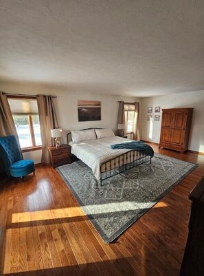 Un dormitorio con cama, una silla azul, un armario de madera y una alfombra.