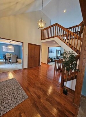 A spacious living area with a wooden staircase, a dining area, and a view into another room. - The Urban Lake House: Near Avalon Grand Resort (Warren)