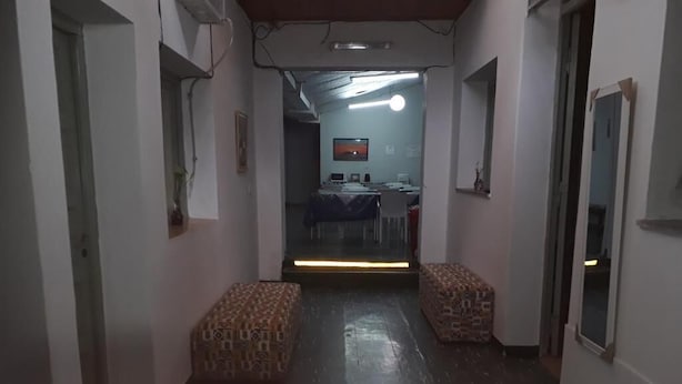 A hallway with patterned benches, a table with chairs, and a room in the background with a table and chairs. - HOSTAL AMALAYA (Salta)