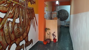 A hallway with a mural of a dinosaur, potted plants, and a circular decorative item on the wall. - HOSTAL AMALAYA (Salta)