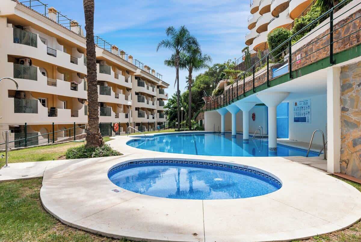 Une piscine de forme circulaire, entourée d’un immeuble à plusieurs étages doté de balcons et d’une façade en pierre.