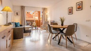 A modern living room with a sofa, a dining table with chairs, a lamp, and a view of a building through a glass door. - Reserva De Marbella apt by Costarentals - Ref M43 (Artola)