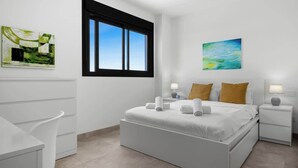A modern bedroom with a large bed, two bedside tables with lamps, a window with blinds, and two wall-mounted paintings.