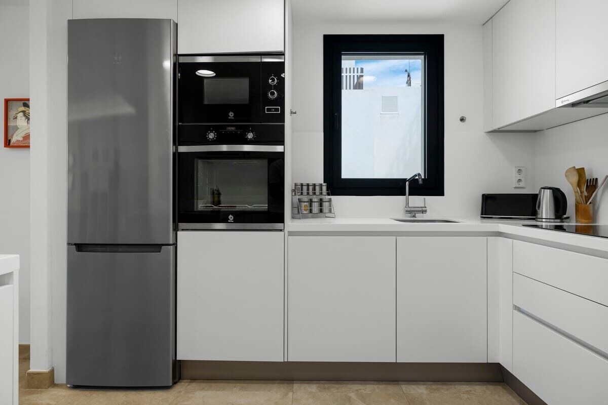 Een moderne keuken met witte kasten, een roestvrijstalen koelkast, een inbouwoven en een raam met uitzicht op de stad.