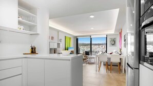 A modern kitchen with white cabinetry, a central island, and a dining area with a view of the city.