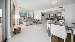 Ein modernes Wohnzimmer mit einer großen Couch, einem Esstisch mit Stühlen und einer Küchenzeile im Hintergrund.
