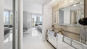 Ein modernes Schlafzimmer mit einem großen Bett, einer Glastür, die auf einen Balkon führt, und einem großen Spiegel mit geometrischem Fliesenrahmen.