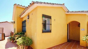 A yellow building with a tiled roof, a window with a metal grille, and a door marked with the number 135.
