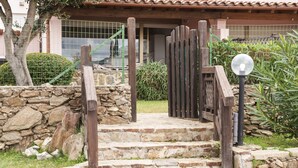 Una escalera de piedra que conduce a una puerta de madera, rodeada de follaje y un muro de piedra.