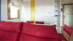 A room with a red sofa, a yellow vertical accent wall, white cabinets, and a door with a handle.