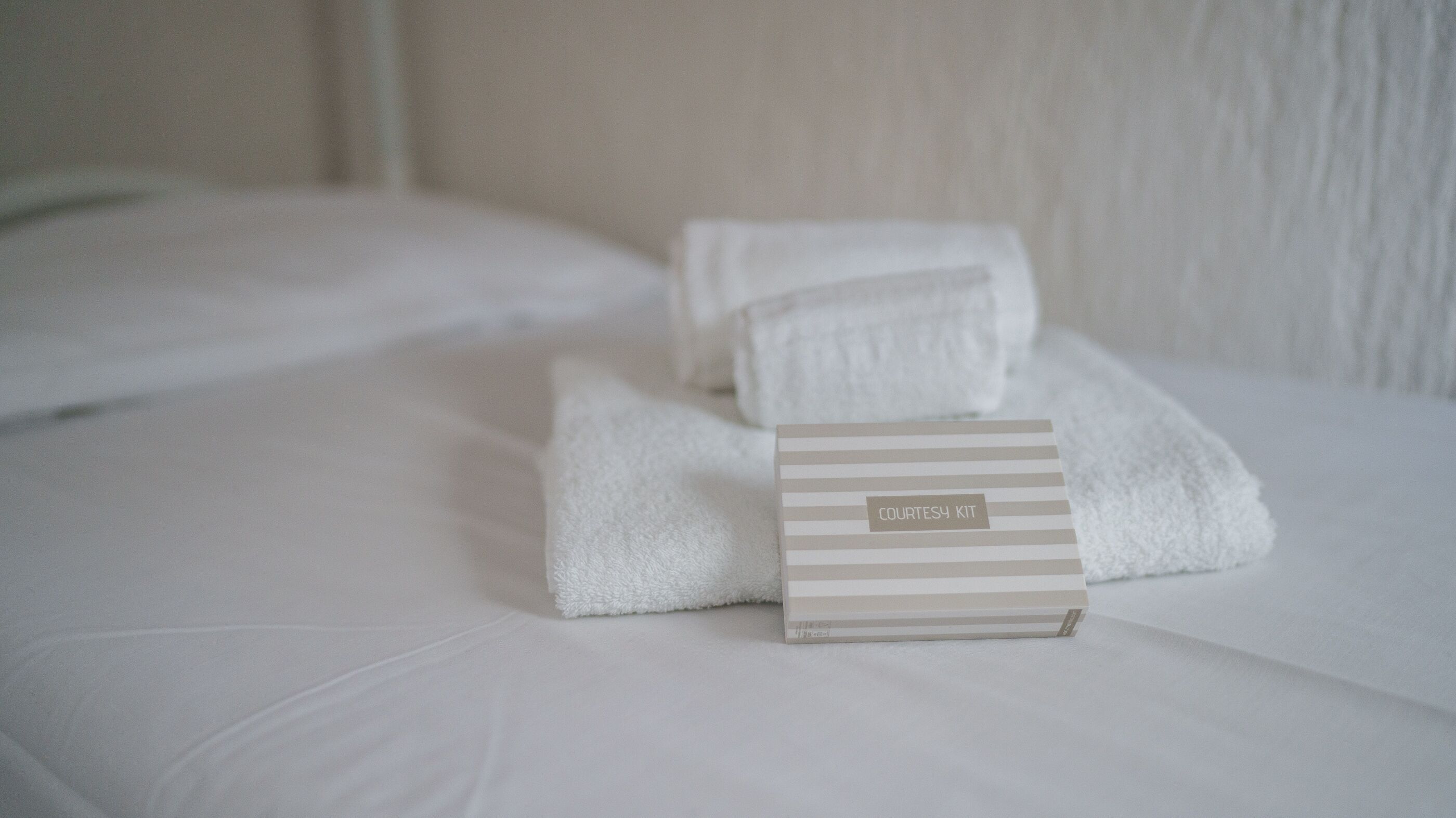 Un lit bien fait, avec du linge de lit blanc et un nécessaire de toilette rayé posé dessus.