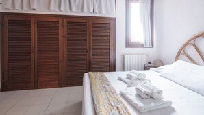 Un dormitorio con cama, ropa de cama blanca, armario de madera y ventana con cortinas.