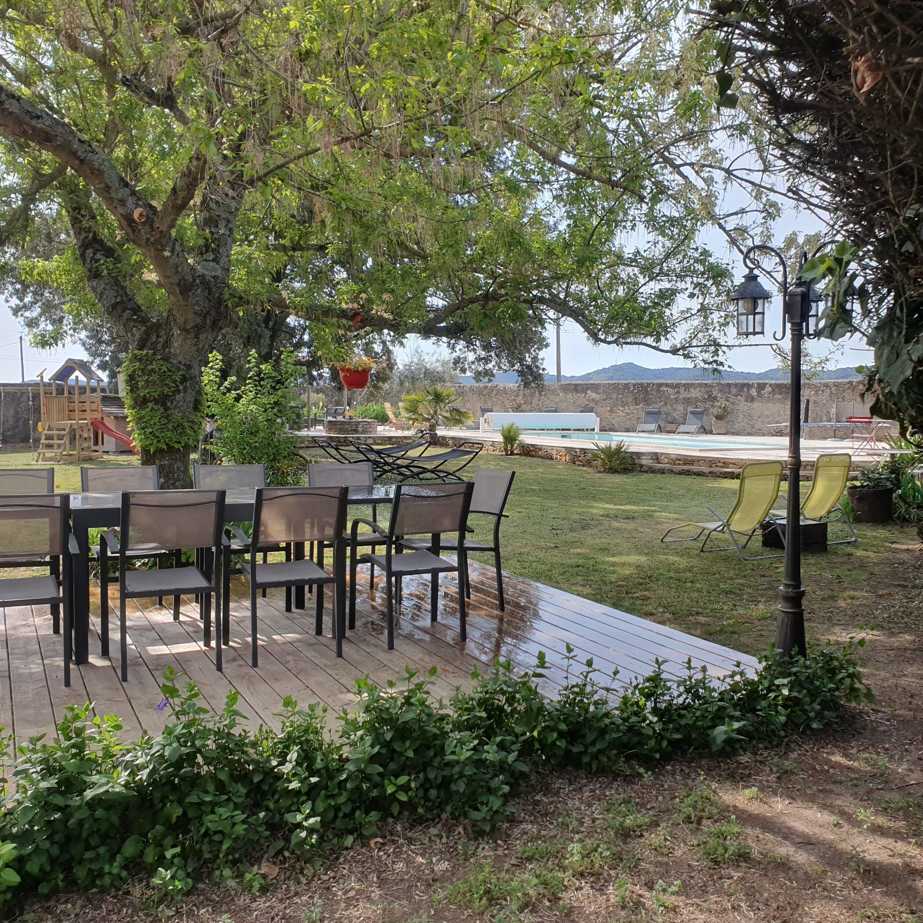 A wooden deck with outdoor furniture, a playground, and a view of a mountainous landscape.