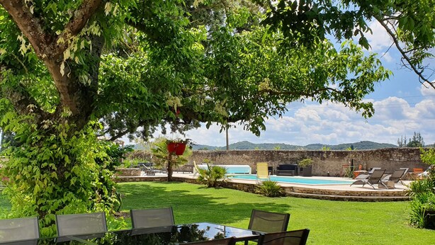 An outdoor patio with a table and chairs, a pool, and a stone wall in the background.
