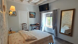 A bedroom with a bed, a desk, a chair, a TV, and a window with curtains.