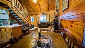 A cozy cabin interior with a wooden staircase, leather sofas, a dining table with wine glasses, and a fireplace. - Visit Mountain Getaway for Labor Day! - Hot Tub - Fiber Wifi - Callaway (Warm Springs)