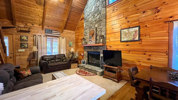 A cozy log cabin interior with a stone fireplace, leather sofa, and a television. - Visit Mountain Getaway for Labor Day! - Hot Tub - Fiber Wifi - Callaway (Warm Springs)