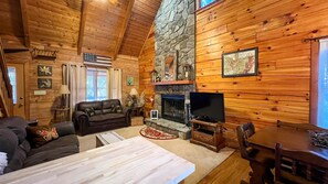 Ein gemütliches Blockhaus-Interieur mit Kamin aus Stein, Ledersofa und Fernseher.