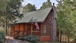 A log cabin with a stone foundation, a porch with a railing, and an American flag. - Visit Mountain Getaway for Labor Day! - Hot Tub - Fiber Wifi - Callaway (Warm Springs)