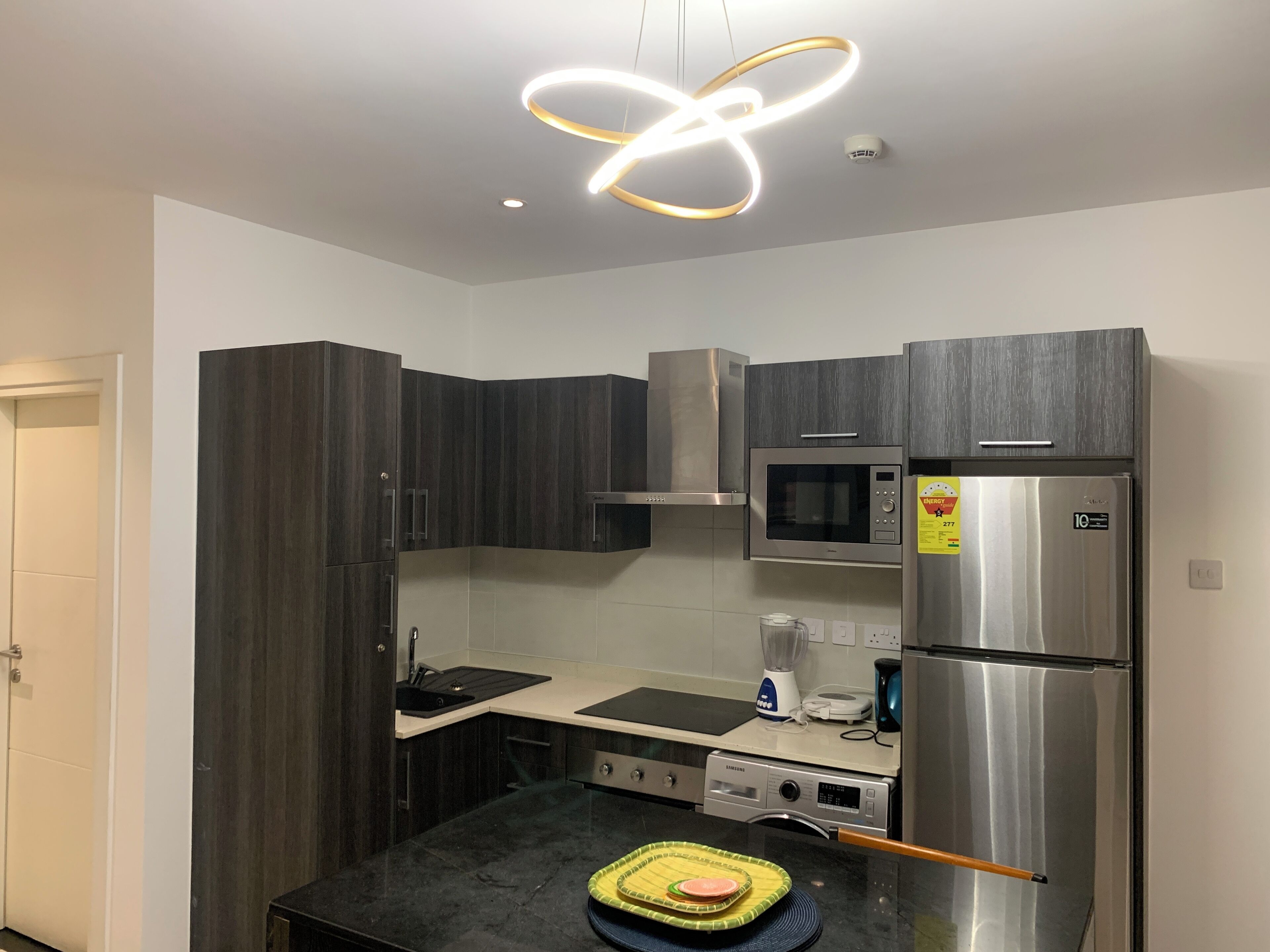 A modern kitchen with dark wood cabinets, a stainless steel refrigerator, a microwave, and a built-in oven.