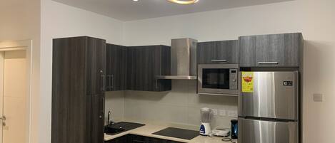 A modern kitchen with dark wood cabinets, a stainless steel refrigerator, a microwave, and a built-in oven.